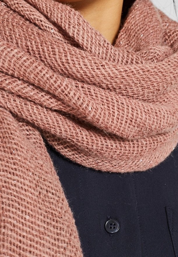 Gros plan d'une écharpe tricotée rose poussiéreux texturée enroulée autour d'une personne portant un vêtement sombre boutonné.