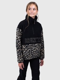 Młoda osoba ubrana w czarny polar w wprint w panterę z napisem "BRUNOTTI", stojąca na jednolitym jasnym tle.