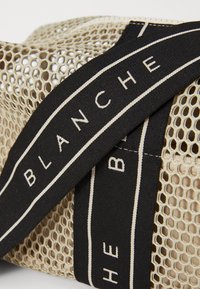 Borsa a rete in beige con finitura texturizzata. Dotata di una tracolla nera con scritte bianche e strisce a contrasto. Design leggero.