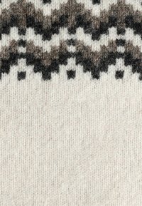 Strickstoff in Creme mit einem geometrischen Muster in Dunkelbraun und Grau. Weiche Textur mit variierenden Maschentiefen, die visuelles Interesse schaffen.
