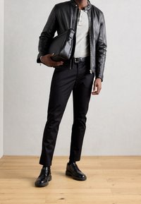 Black leather jacket, gray henley shirt, black pants, black shoes, and a black messenger bag, set against a light textured background.