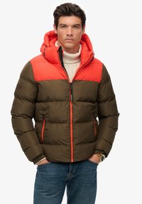 Padded jacket with an olive green body and bright orange shoulders. Features a hood, zippered pockets, and a textured knit sweater underneath.