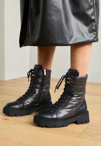 Bottines en cuir noir avec un dessus matelassé texturé, un design à lacets et une semelle en caoutchouc épaisse avec des accents décoratifs.