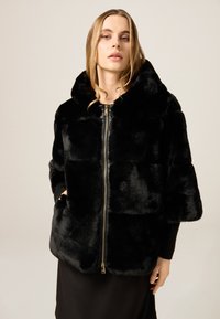 Czarna kurtka z imitacji futra z kapturem, zapinana na zamek, o pudełkowatym kroju, z prążkowanym materiałem przy mankietach. Miękka w dotyku, bez wzorów.