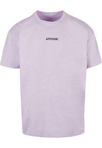 Camiseta de algodón de color morado claro con mangas cortas y cuello redondo. "ACTITUD." impreso en negrita en negro en el centro del frente.