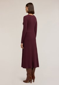 Abito a maglia ribbed color bordeaux con maniche lunghe, corpino aderente e gonna svasata. Indossato con stivali alti color marrone con tacco.
