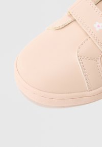 Ροζ παιδικό παπούτσι από λείο συνθετικό υλικό, με στρογγυλεμένη μύτη και λουράκι με βέλκρο που φέρει ένα μικρό λουλουδάτο σχέδιο.