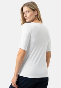 Wit T-shirt met korte mouwen van zacht materiaal, met een ronde hals en een slimfit ontwerp. Eenvoudige, naadloze constructie zonder patronen.