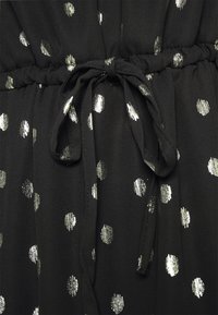 Tissu noir à pois argentés métalliques avec un cordon noué à la taille froncée.
