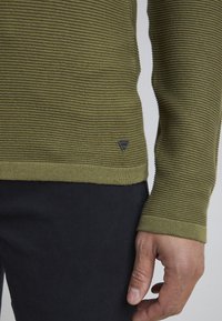 Pulover tricotat de culoare verde măsliniu, cu dungi orizontale texturate, croială slim, cu manșete și tiv din tricot, având un mic eticheta neagră logo pe lateral.