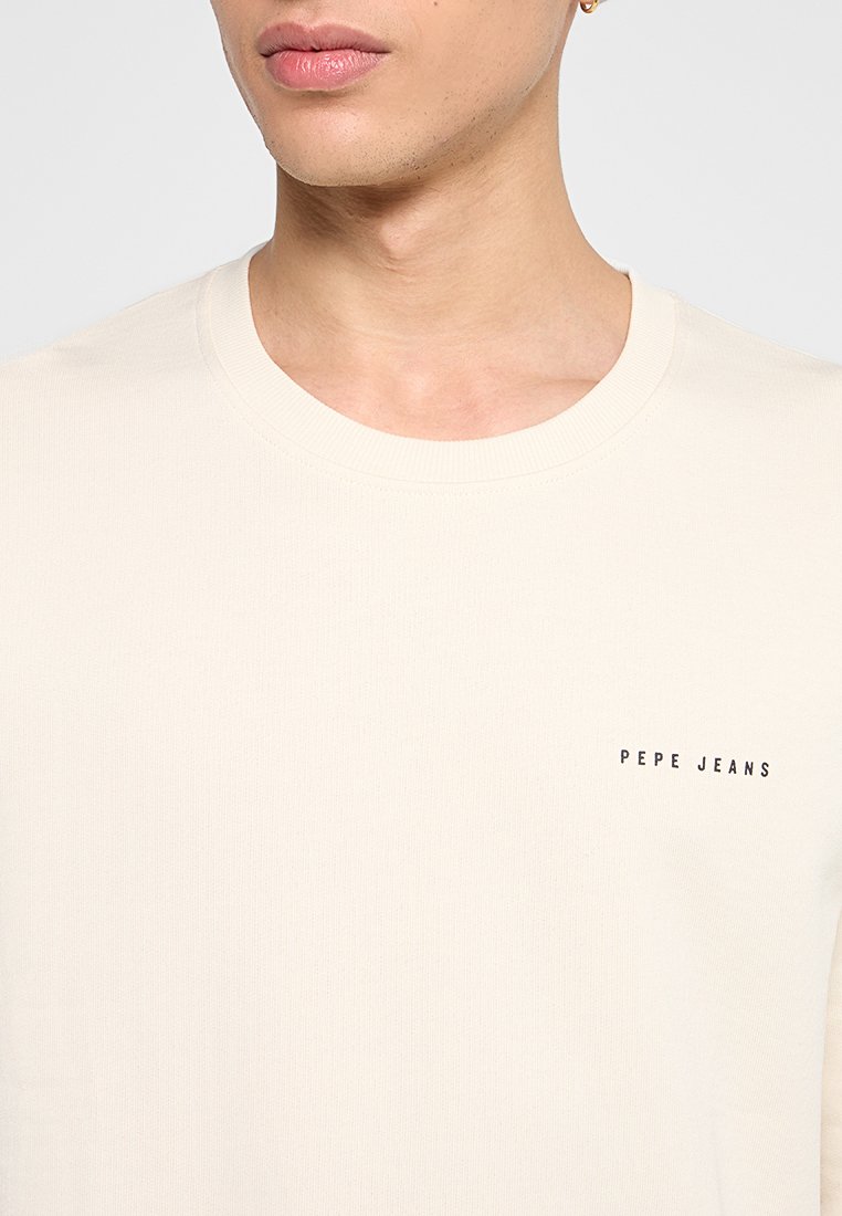 Cremfarbendes T-Shirt mit kurzen Ärmeln, ribbeliger Textur und kleinem schwarzen "PEPE JEANS"-Logo auf der linken Brust. Runde Ausschnitt.