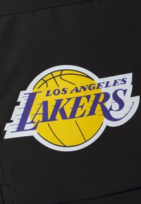 Crni tkaninski prostor s okruglim logom na kojem je žuta košarka i tekst "LOS ANGELES LAKERS" u ljubičastoj boji.