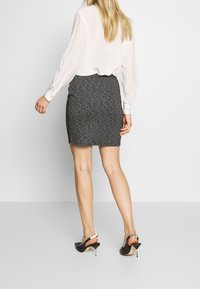 Falda lápiz de patrón en blanco y negro con un acabado texturizado, combinada con una blusa blanca de manga larga y tacones negros de tipo slingback.
