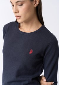 Maglione a girocollo blu navy realizzato in tessuto morbido, con un piccolo logo rosso ricamato sul petto. Design aderente con una texture liscia.