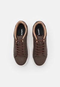 Brune lærersneakers med en teksturert finish, med beige fôr og brune snørebånd. Hvit gummisåle, logo synlig på tungen.