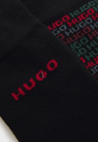 Schwarzer Stoff mit rotem "HUGO"-Text auf einer Seite und einem mehrfarbigen wiederholten "HUGO"-Muster auf der anderen Seite.