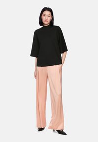 Black short-sleeve top paired with light pink wide-leg trousers, featuring a sleek design and a smooth texture, complemented by black heels.