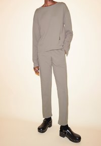 Sweat-shirt gris à manches longues avec un col rond et un pantalon gris assorti. Le mannequin porte des sabots noirs ornés de clous argentés. Texture lisse.