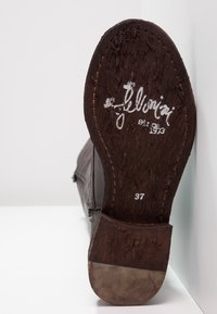 Suela de zapato de cuero marrón con madera texturizada, con escritura metálica y talla "37". El tacón tiene un acento de color claro en la parte inferior.