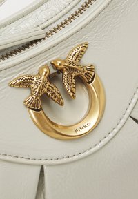 Borsa in ecopelle bianca con chiusura a motivo di uccello dorato, forma arrotondata, superficie testurizzata e dettagli visibili della cerniera.