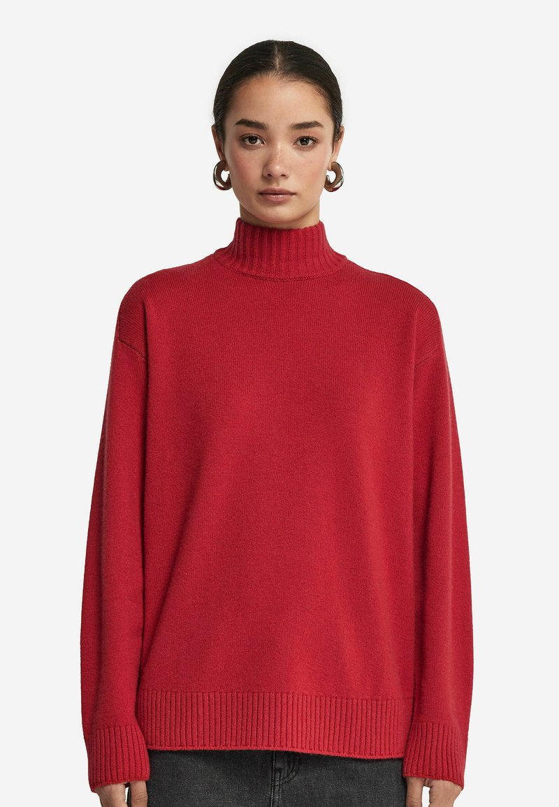Roter, gerippter Rollkragenpullover mit lässiger Passform, langen Ärmeln und texturiertem Finish, kombiniert mit einem minimalistischen Design.