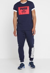 Mörkblå bomullströja med vita detaljer och en röd tryckt logotyp; matchad med mörkblå joggers med en vit logotyp längs benet.