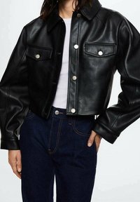 Zwarte cropped leren jas met een kraag, drukknoopsluiting en twee borstzakken. Gladde textuur, minimale stikseldetails.