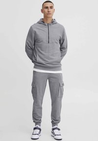 Gray hooded sweatshirt with a front pocket, paired with matching cargo pants featuring side pockets and elastic cuffs. White sneakers.