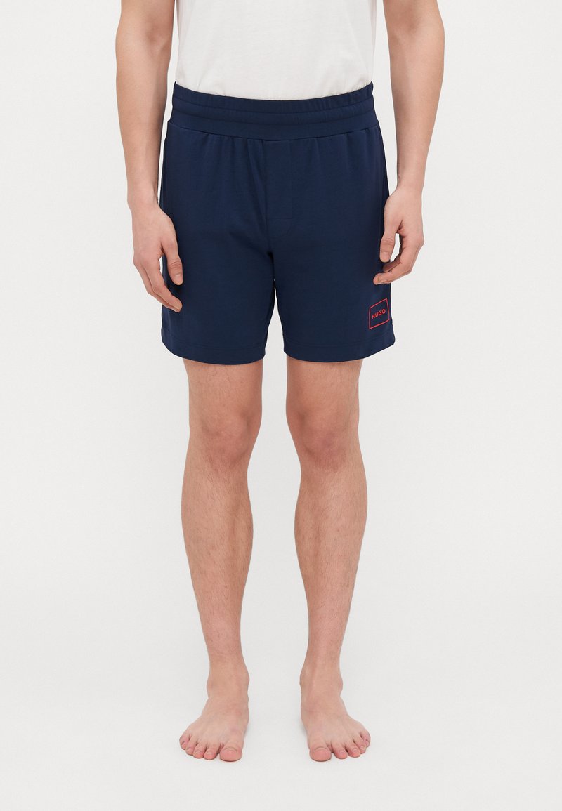 Mørkeblå shorts med elastisk midje og en liten rød logodetalj. Laget av et glatt stoff, med et enkelt, klassisk design.