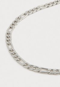 Collier en chaîne en métal argenté avec un design de maillons entrelacés. Texture lisse avec une finition polie ; présente des maillons allongés et arrondis.