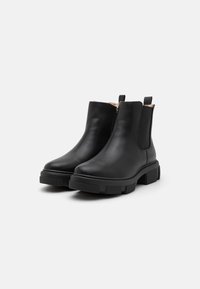 Bottines en cuir noir avec une finition lisse, des panneaux élastiques sur les côtés et une semelle en caoutchouc épaisse et texturée. Comprend des languettes pour un enfilage facile.