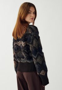 Megztinis tamsiomis spalvomis su geometriniais raštais. Yra apvadu ir laisvas kirpimas. Minkšta tekstūra su skirtingomis spalvų atspalviais.