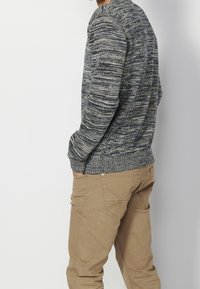 Pull tricoté en marine et gris, avec un motif texturé, un col rond et des poignets côtelés, accompagné d'un pantalon beige.