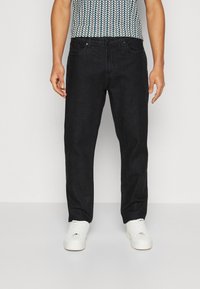 Jean en denim noir avec une coupe droite, un design à cinq poches et des détails de couture subtils. Associé à des baskets blanches et une chemise à motifs.