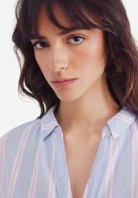 Camicia colletto azzurro chiaro con righe verticali rosa e bianche. Tessuto morbido, vestibilità comoda, cuciture e dettagli del colletto visibili.