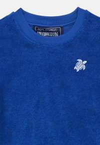 Sudadera de algodón azul con tejido texturizado, cuello redondo y un logo bordado de tortuga en el pecho izquierdo. Diseño suave y casual.