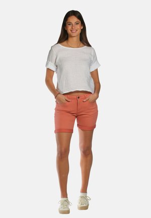 Haut en lin blanc coupé avec des manches roulées, associé à un short corail avec un ourlet retroussé. Modèle portant des baskets décontractées.