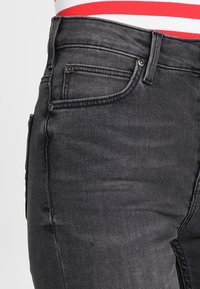 Svarta denimjeans med en figurnära silhuett, femficksdesign och en subtil textur med synliga sömdetaljer.