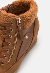 Botte d’hiver marron avec laçage à l’avant, fermeture éclair latérale et doublure en polaire bouclée autour de la cheville.