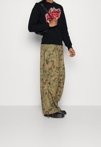 Sudadera negra con gráfico rojo, pantalones cargo de camuflaje y zuecos negros, con un ajuste relajado y bolsillos visibles.