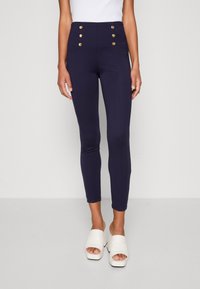 Vysoké námořnické legíny s zlatými knoflíkovými akcenty, přizpůsobený střih a elastický materiál. V kombinaci s otevřenými bílými podpatky.