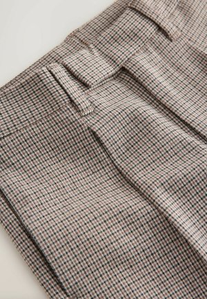 Zbliżenie złożonych spodni w brązowo-beżowy wzór houndstooth z szlufkami na pasek i kantami na beżowym tle.