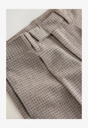 Pogled od blizu na nabrane houndstooth hlače v rjavi in bež barvi z zankami za pas in nabrane, na bež ozadju.