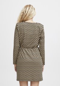 Musta ja beige ruudullinen mekko pitkähihalla, sivusolmukeydellä ja vartalonmyötäisellä siluetilla, valmistettu sileästä kankaasta.