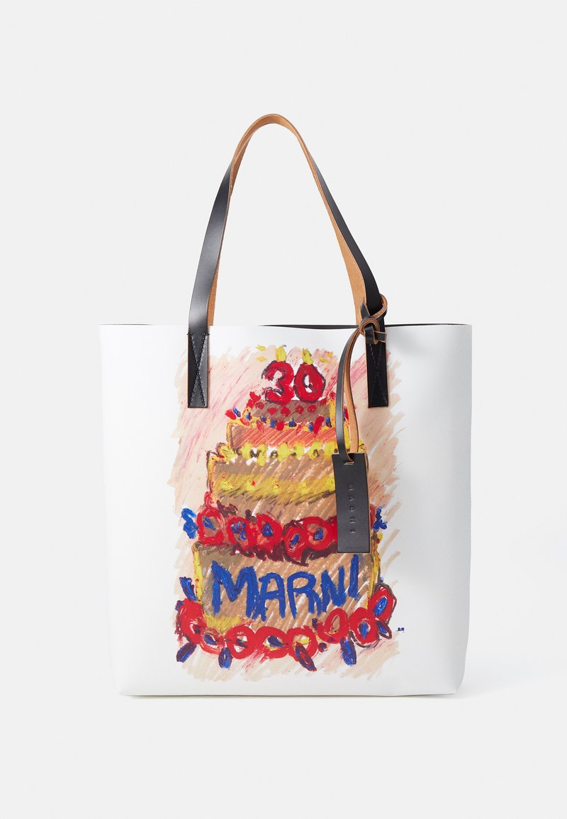 Sac de toile blanc avec une illustration colorée de gâteau d'anniversaire, des anses en cuir noir et une étiquette en cuir marron portant le nom "Marni."