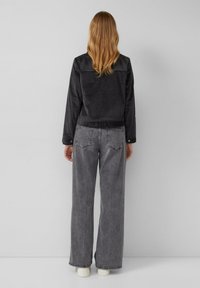 Zwarte corduroy jasje met een cropped ontwerp, met een knoopsluiting aan de voorkant en een gebande onderkant, gecombineerd met grijze wijde jeans.