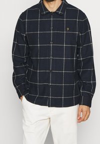 Camicia a quadri blu navy con linee bianche, realizzata in un tessuto testurizzato, con colletto e un piccolo logo sul petto.