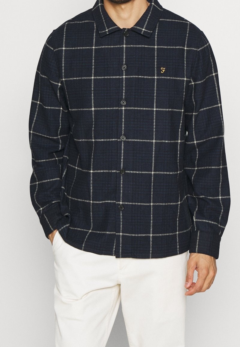Camicia a quadri blu navy con linee bianche, realizzata in un tessuto testurizzato, con colletto e un piccolo logo sul petto.