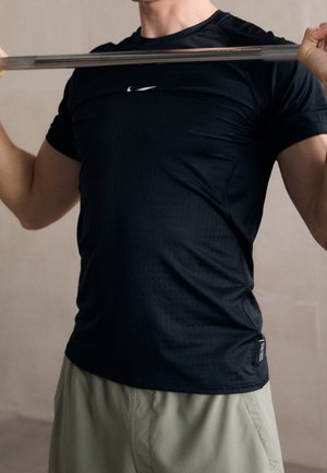 Person trägt schwarzes Nike-Shirt und hebt eine Langhantel auf Schulterhöhe, der Fokus liegt auf Oberkörper und Armen.