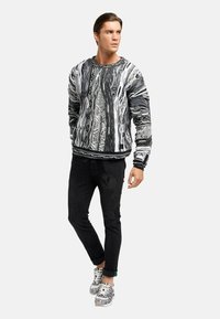 Sorte og hvide mønstrede sweatshirts med varierende teksturer, båret med sorte bukser og mønstrede sneakers. Har rund hals og ribbede manchetter.